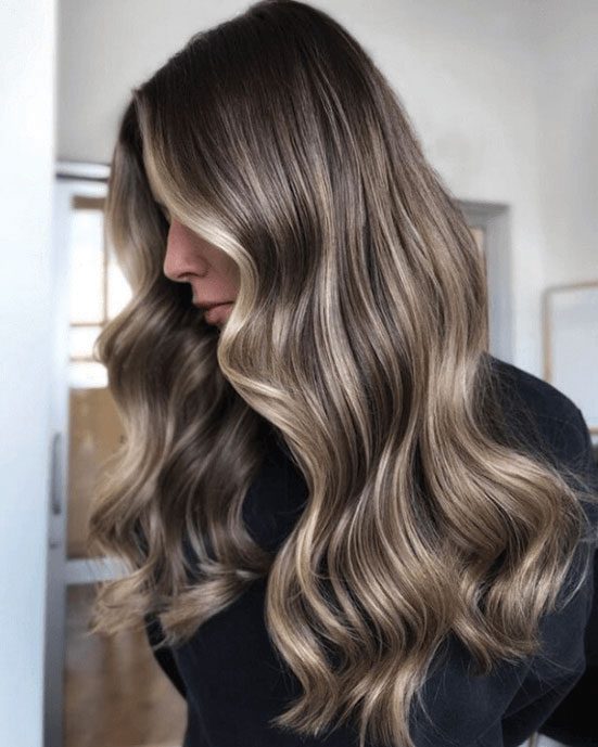Side view of shoulder-length wavy hair with dark roots and bright beige-blonde face-framing balayage
