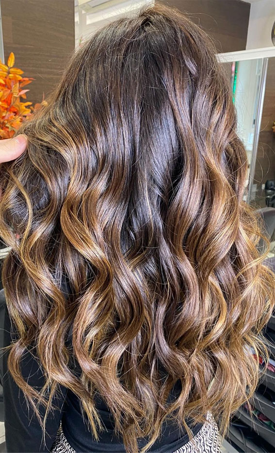 Woman with defined curls in warm cinnamon caramel brown balayage