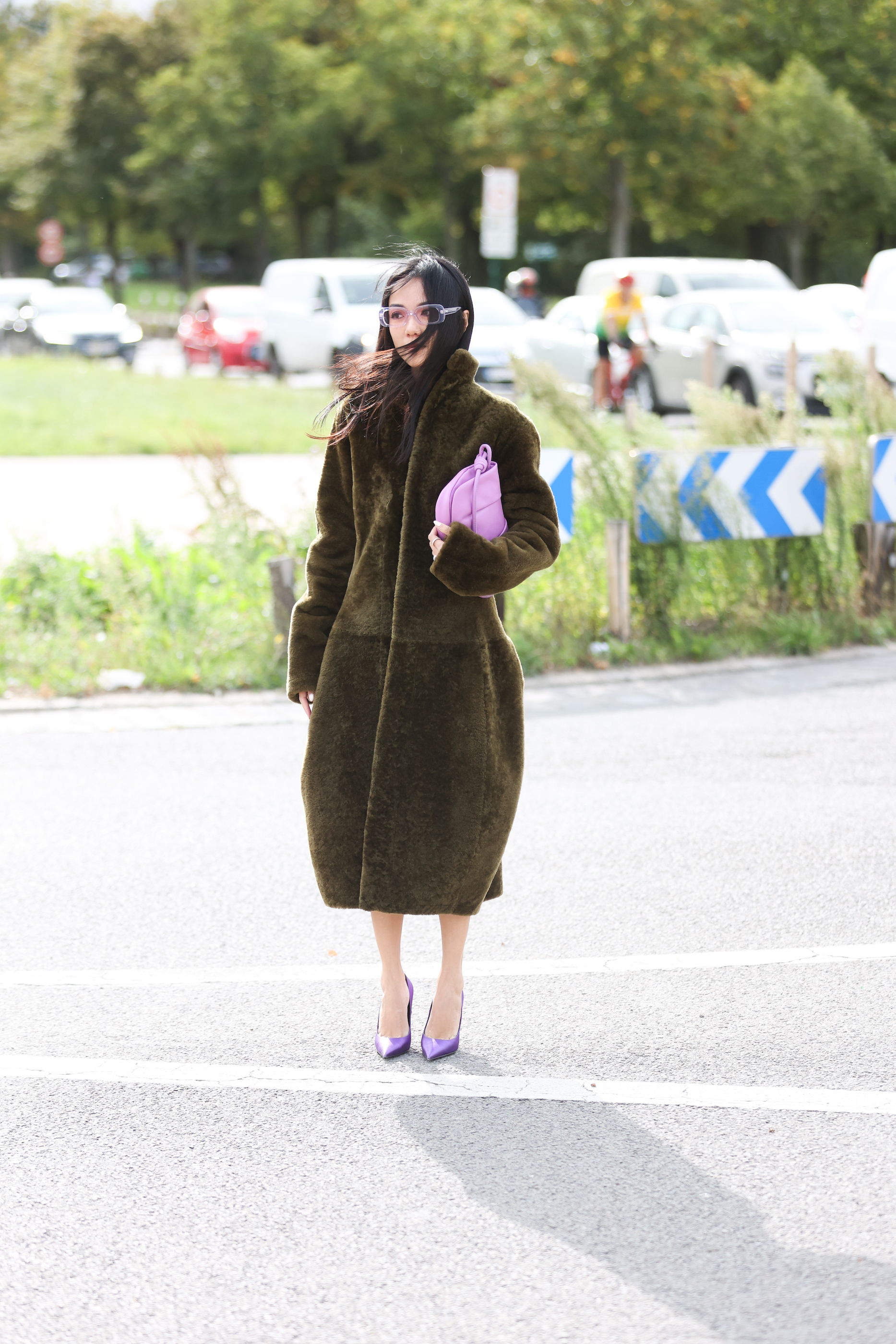 Woman in an olive shearling coat with a lilac bag and purple heels at Paris fashion week