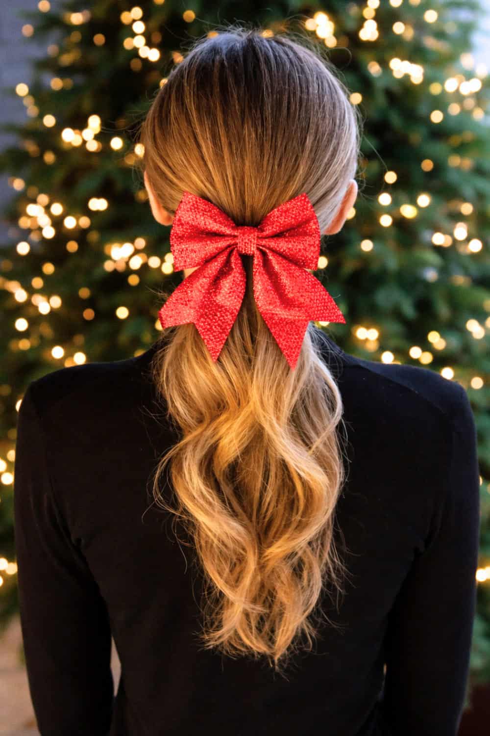 Low softly waved ponytail finished with a bold red bow at the nape