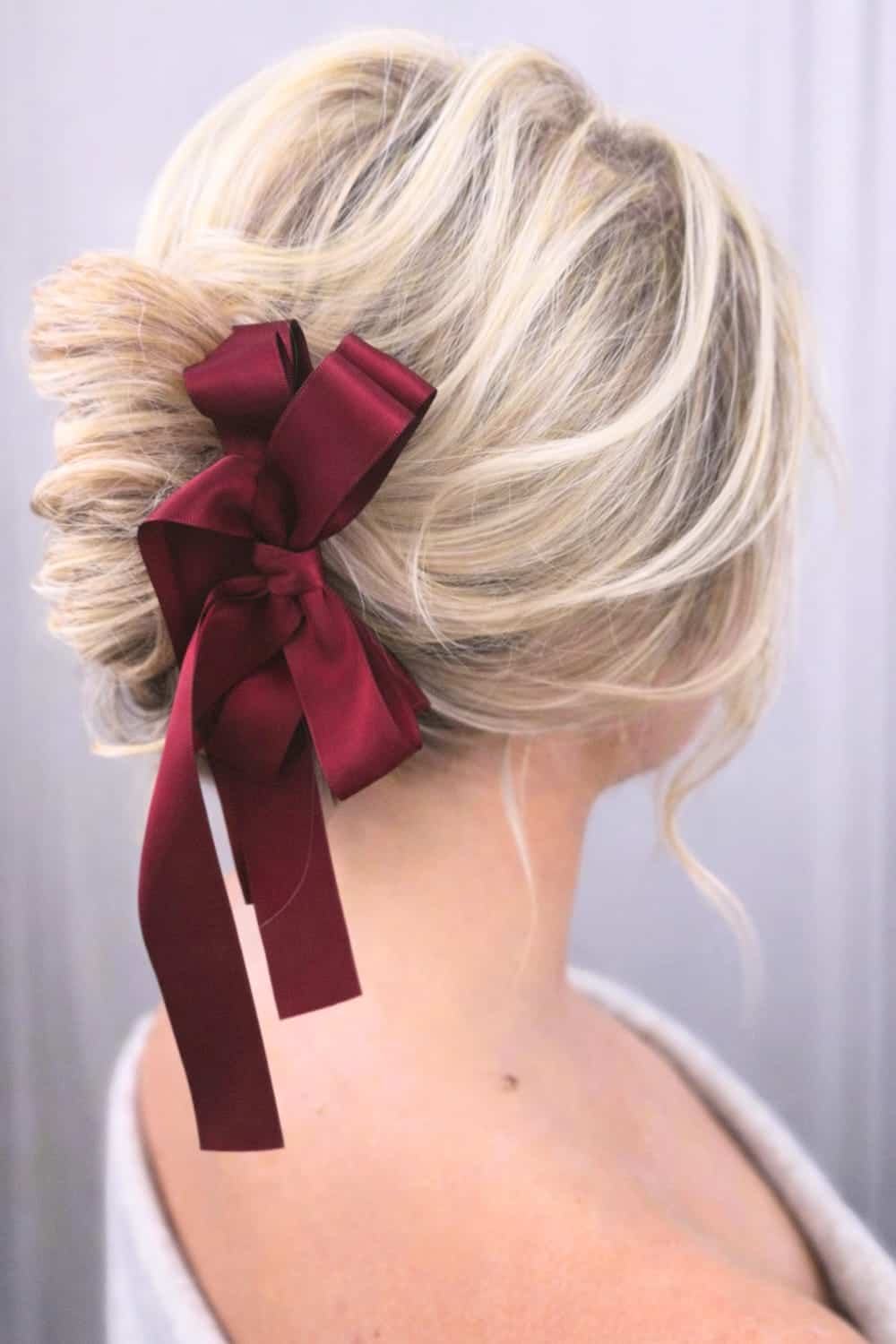 Soft slightly messy low bun with loose face-framing pieces and a long red satin bow