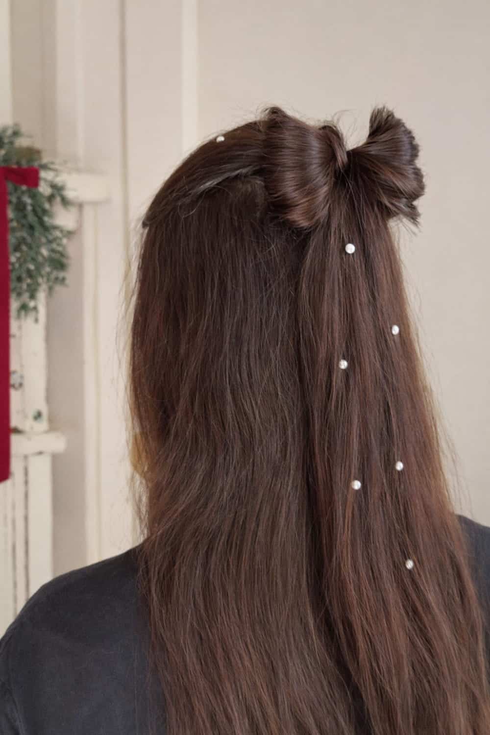 Half-up hairstyle with hair tied into a small bow-shaped bun and pearl pins through long hair