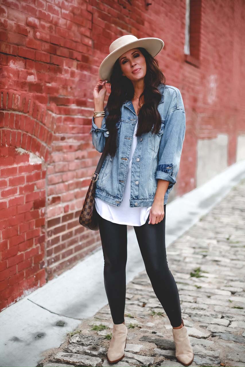 Woman wearing an oversized denim jacket with black leggings, beige ankle boots and a fedora hat