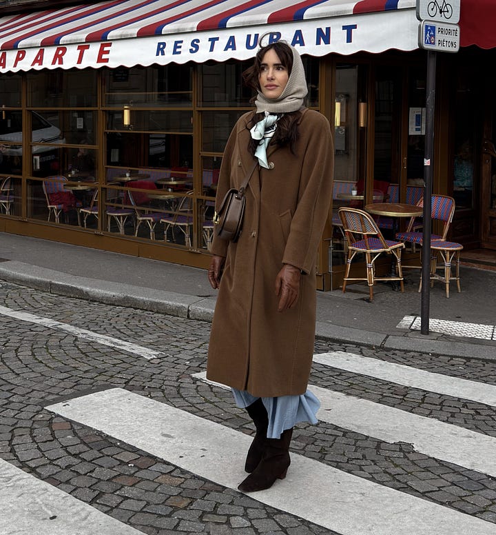 Woman in a camel wool coat, cream knit headscarf, leather gloves and blue skirt on a Paris street