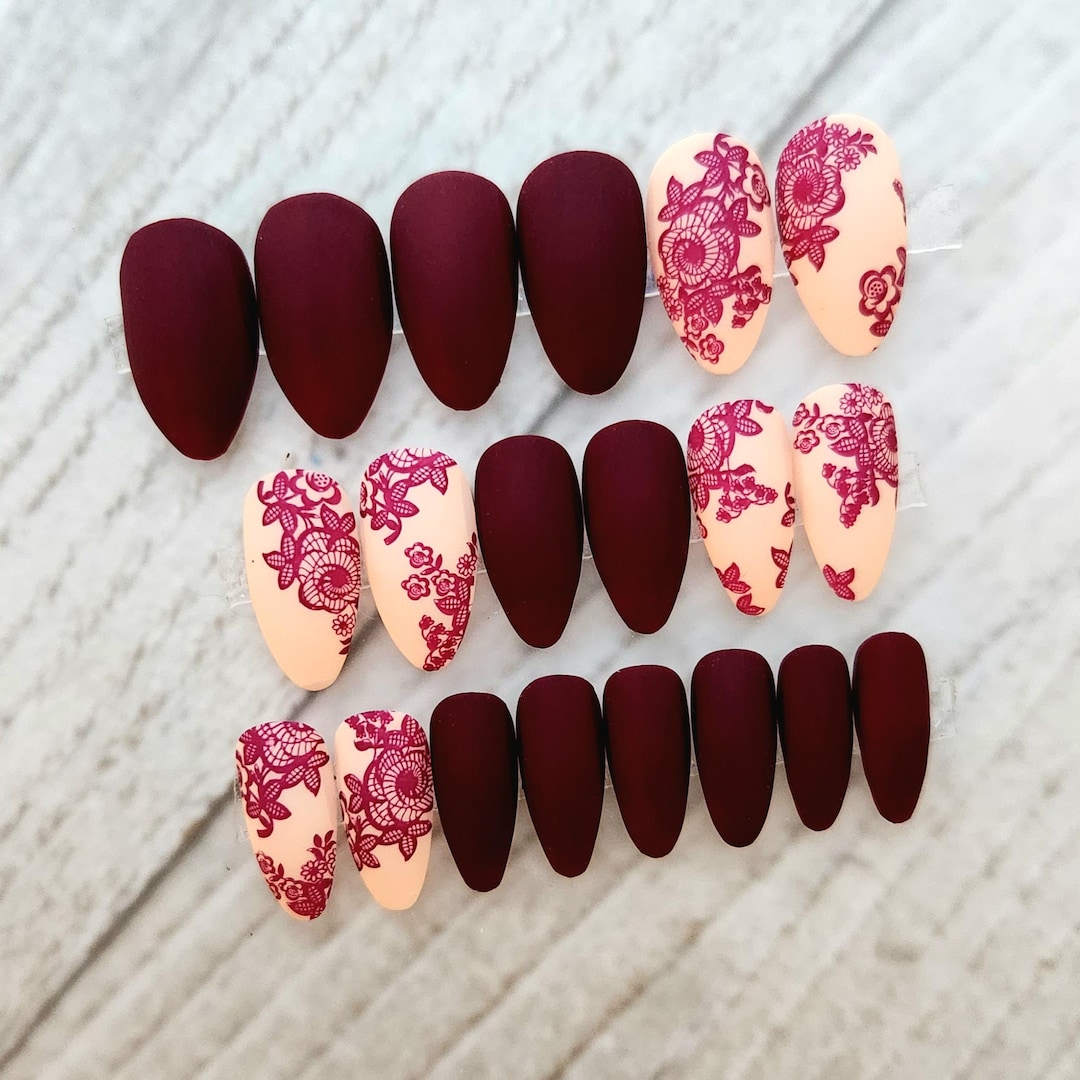 Matte burgundy almond nails with wine-red floral lace pattern on nude accent nails