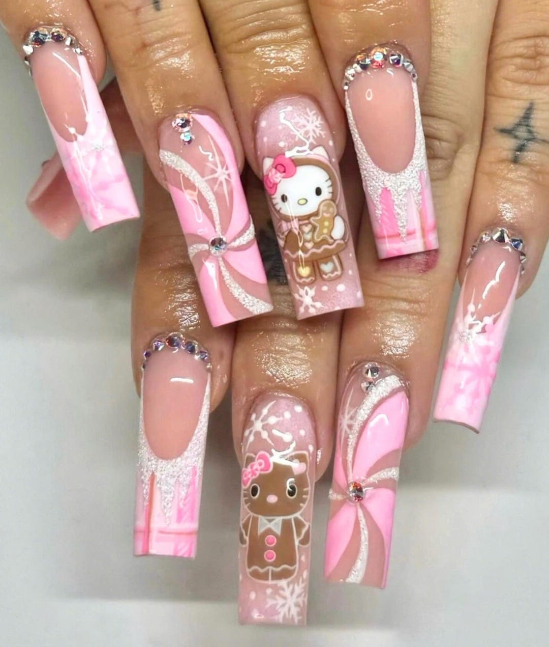 Long square nails in pink and white with Hello Kitty as a gingerbread cookie, peppermint swirl bows and rhinestone cuticle lines