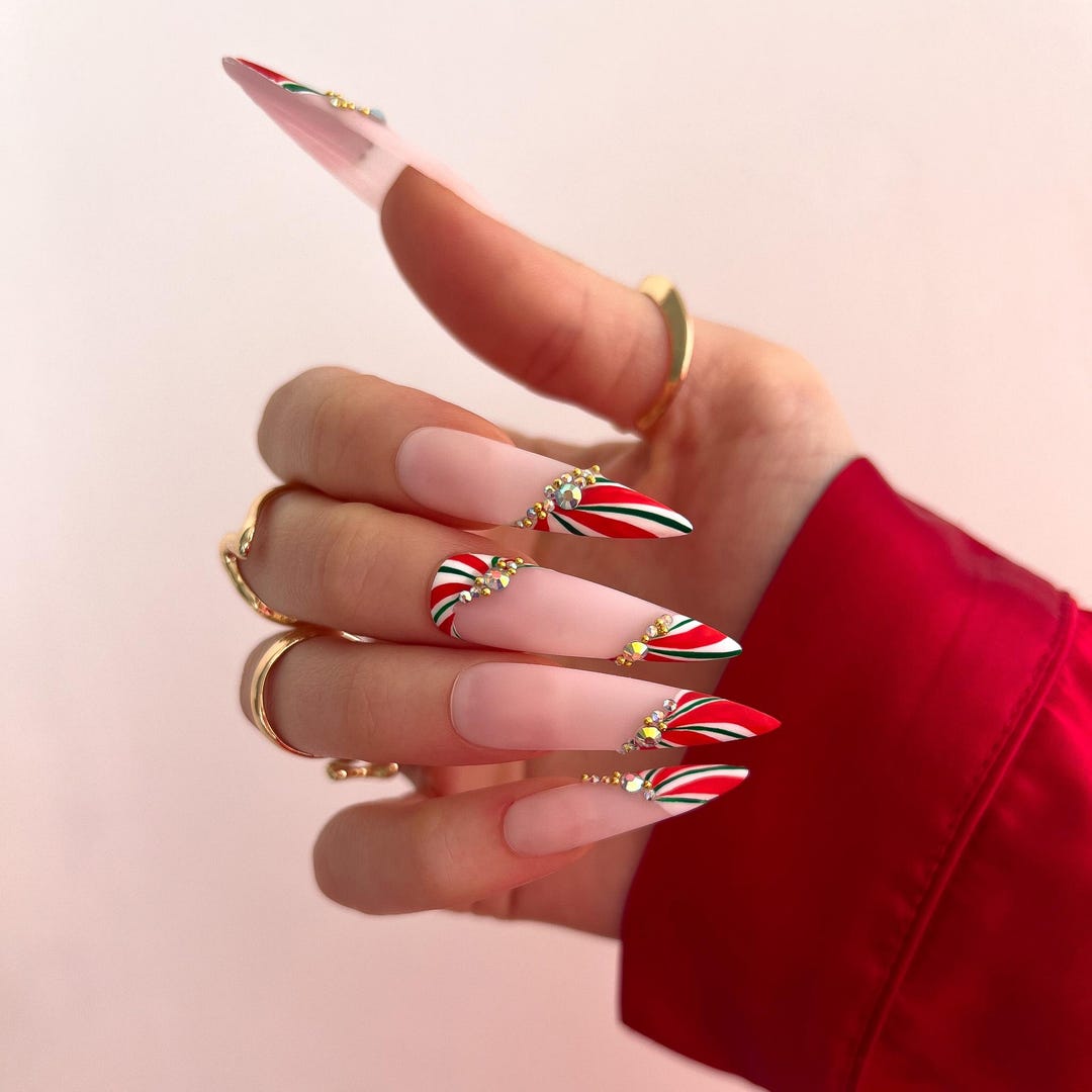 Nude stiletto nails with red and green candy cane striped tips and crystal accents