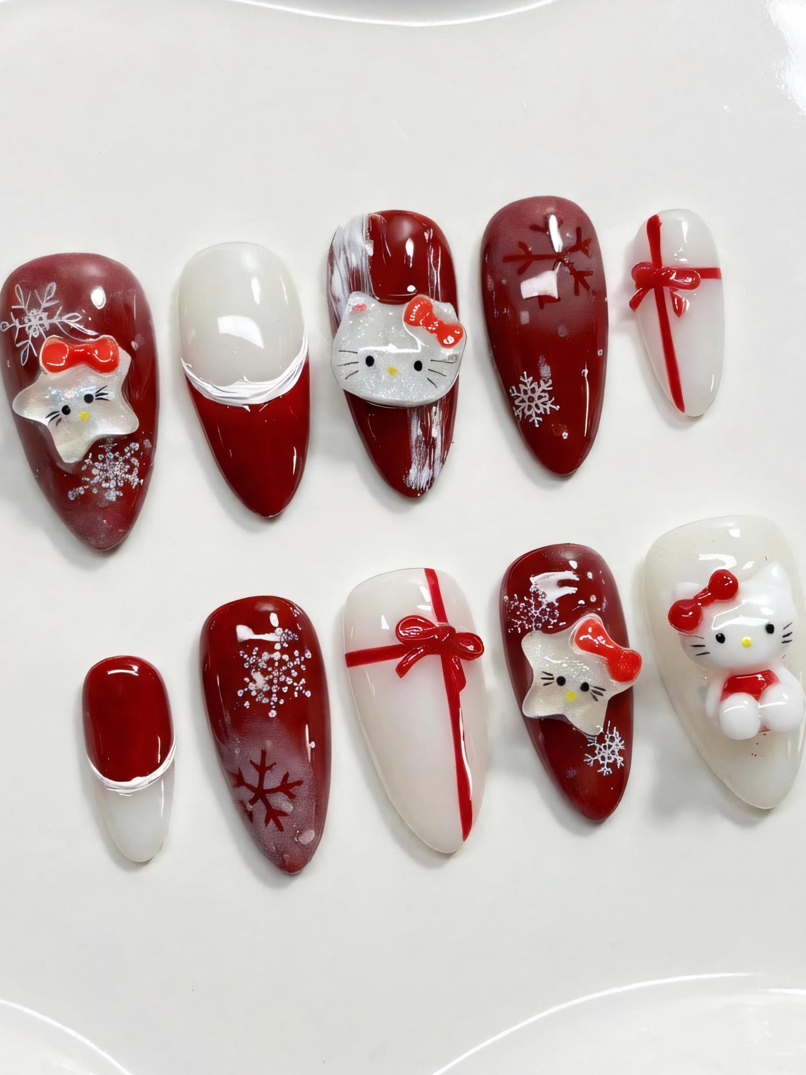 Long almond press-on nails in deep red and milky white with 3D Hello Kitty faces, red bows and snowflake decals