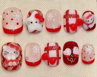 Short squoval press-on nails in red and white with Hello Kitty faces, snowflakes, gift wrap patterns and a reindeer