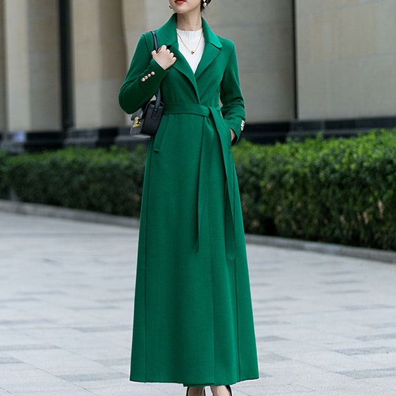 A bright kelly green belted long coat over a white top with a black shoulder bag.