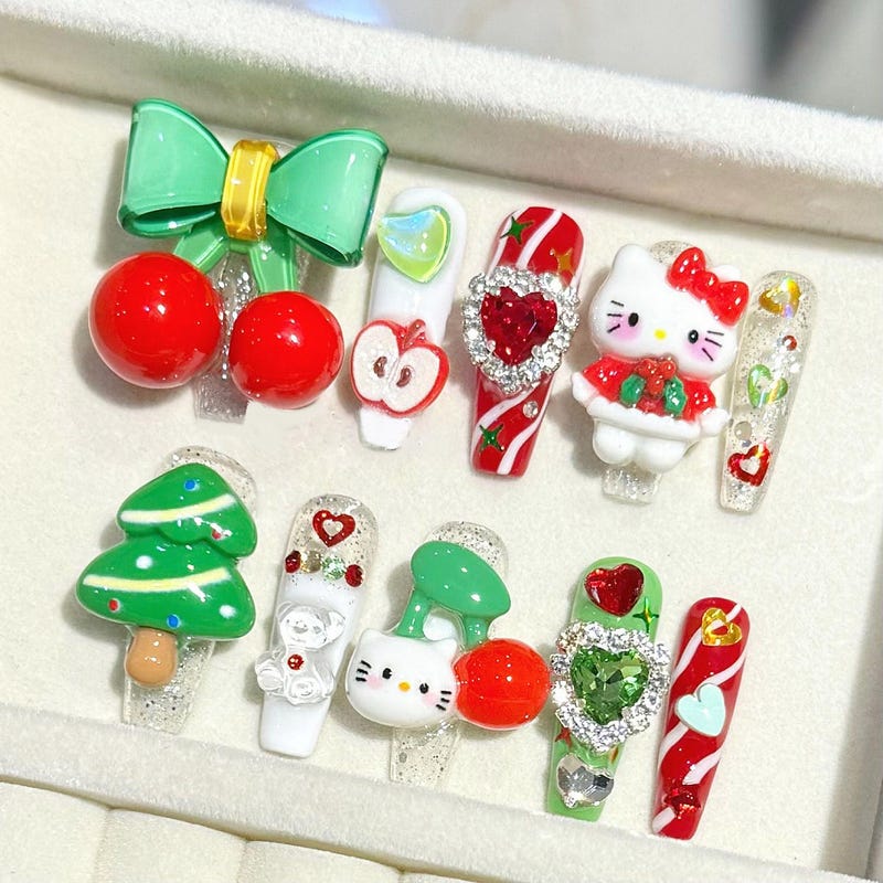 Long coffin press-on nails with 3D sculptural art: a giant green bow with red cherries, a green Christmas tree, Hello Kitty faces, candy cane swirls and rhinestone hearts