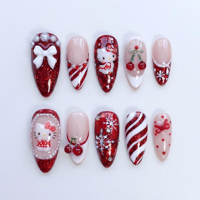 Medium almond press-on nails in red glitter with Hello Kitty in a red dress, candy cane swirls, red cherries, snowflakes and a white bow with pearls