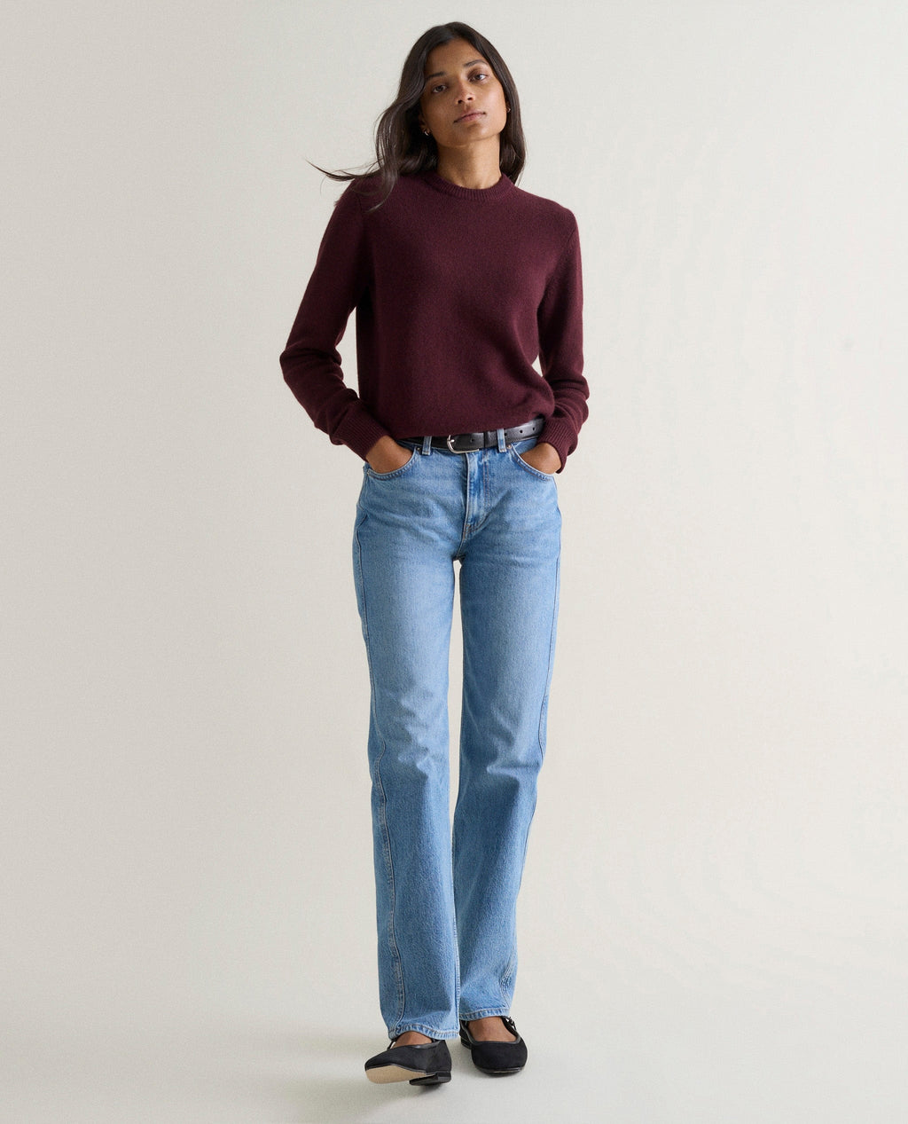 Woman wearing an oxblood burgundy cashmere sweater with straight-leg blue jeans