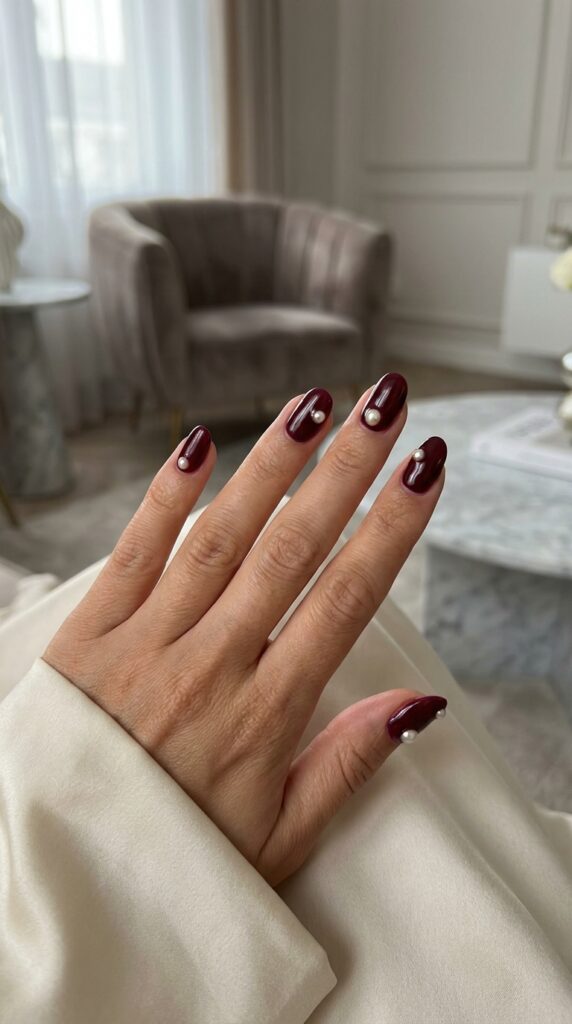 Short oval nails in glossy wine red with small pearl accents on each nail