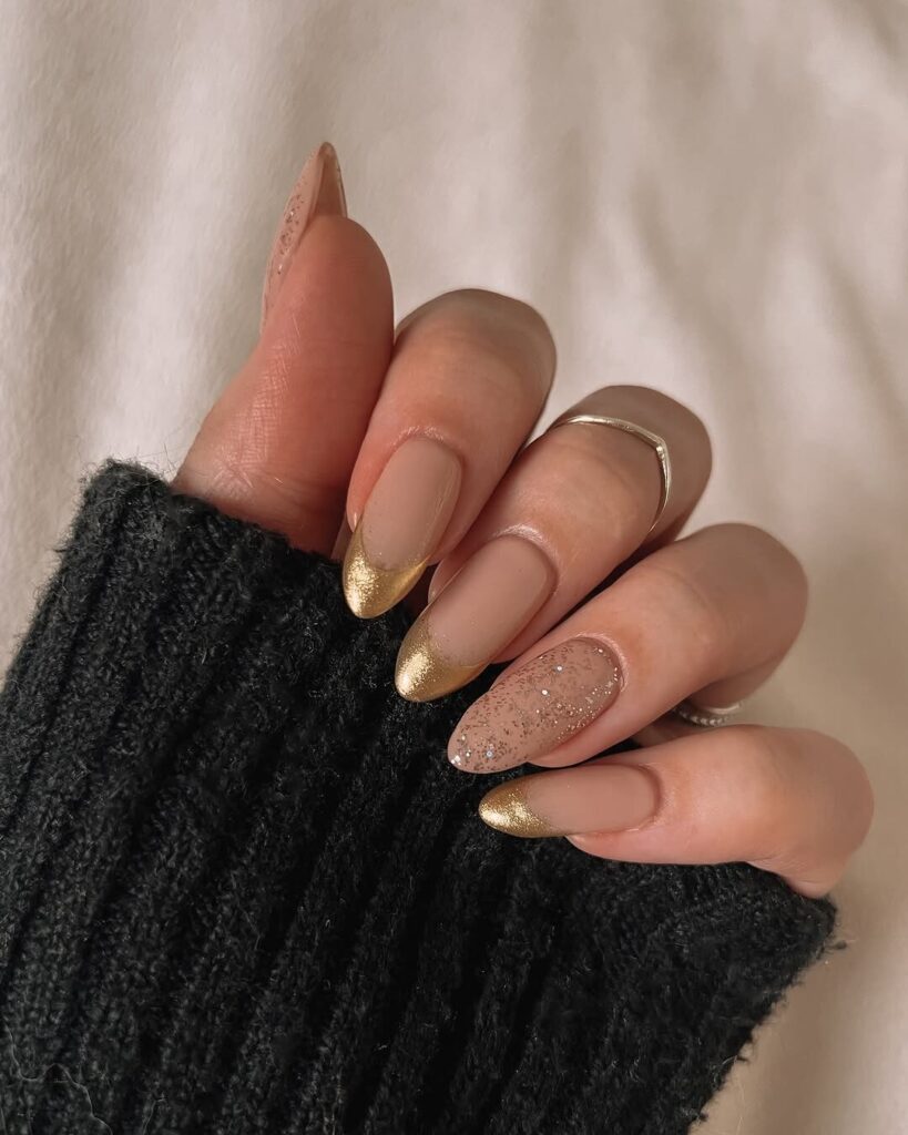 Nude almond gel nails with gold French tips and a gold glitter accent nail