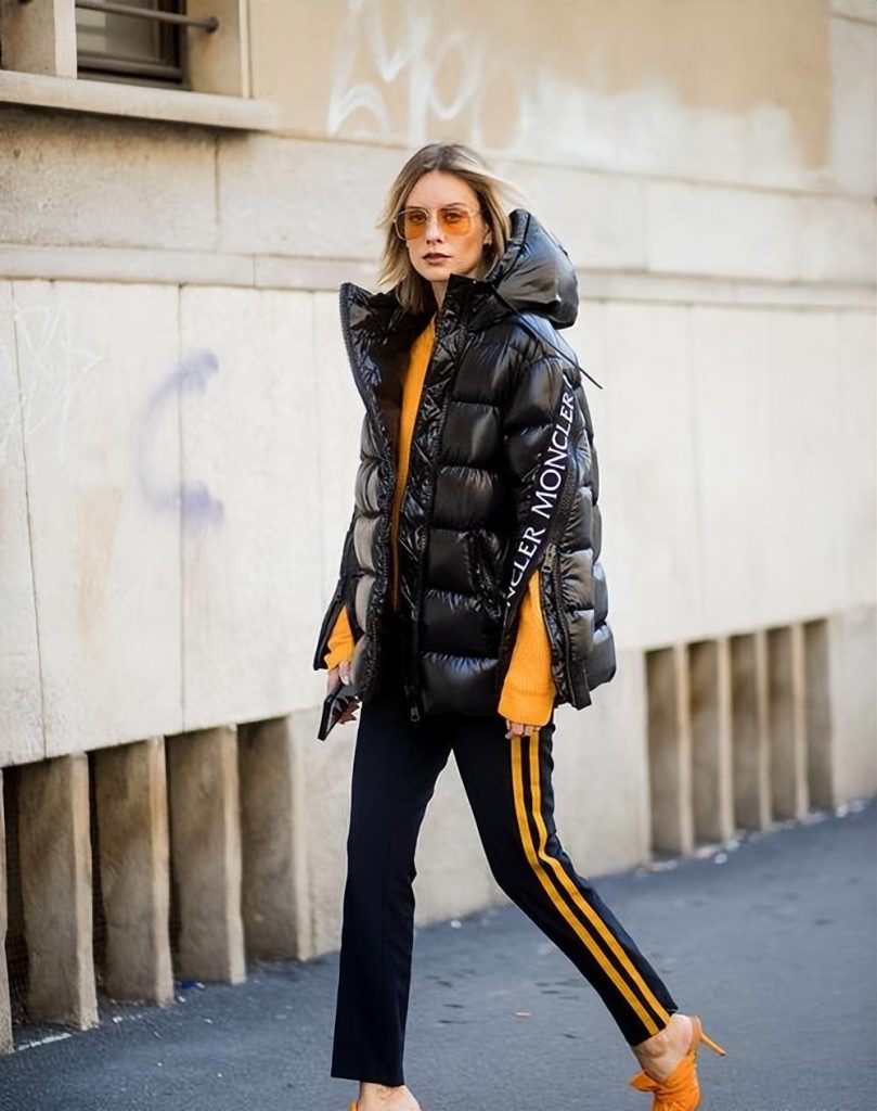 Woman in a black cropped puffer with a mustard knit and striped track pants