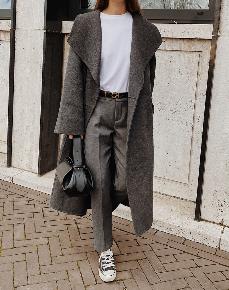 A charcoal grey long coat over a white tee, grey trousers, black belt, black bag and sneakers.