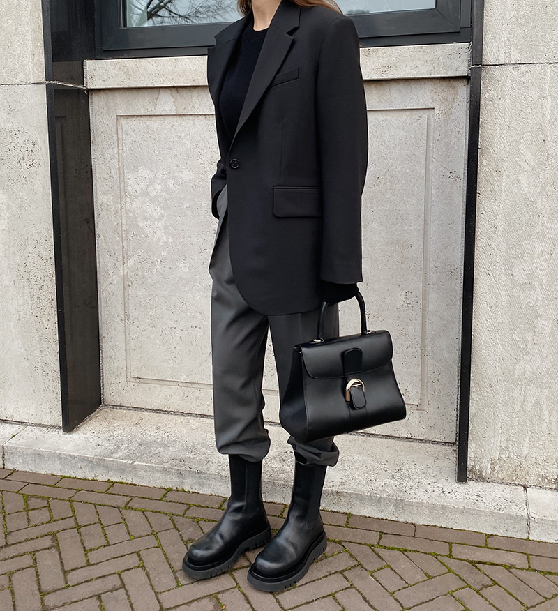 Woman in black chunky Chelsea boots, grey tailored trousers, black blazer and structured handbag