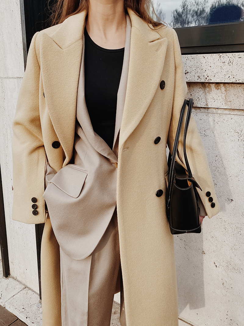 Woman wearing a camel blazer and matching camel trousers layered under a camel coat, tone-on-tone