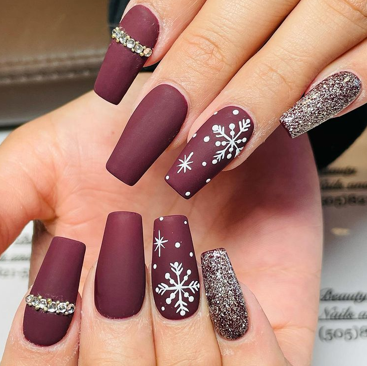 Matte burgundy coffin nails with white snowflake art, silver glitter and rhinestone accents