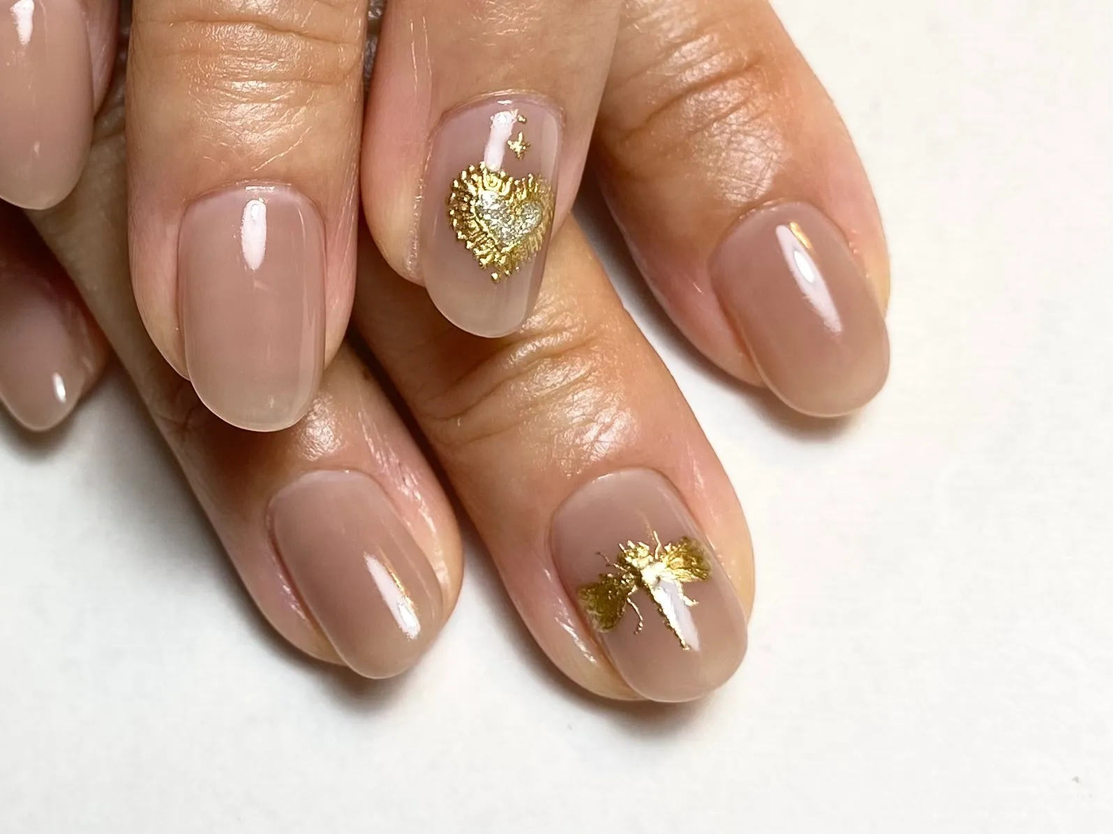 Nude manicure with gold foil heart accents on short nails