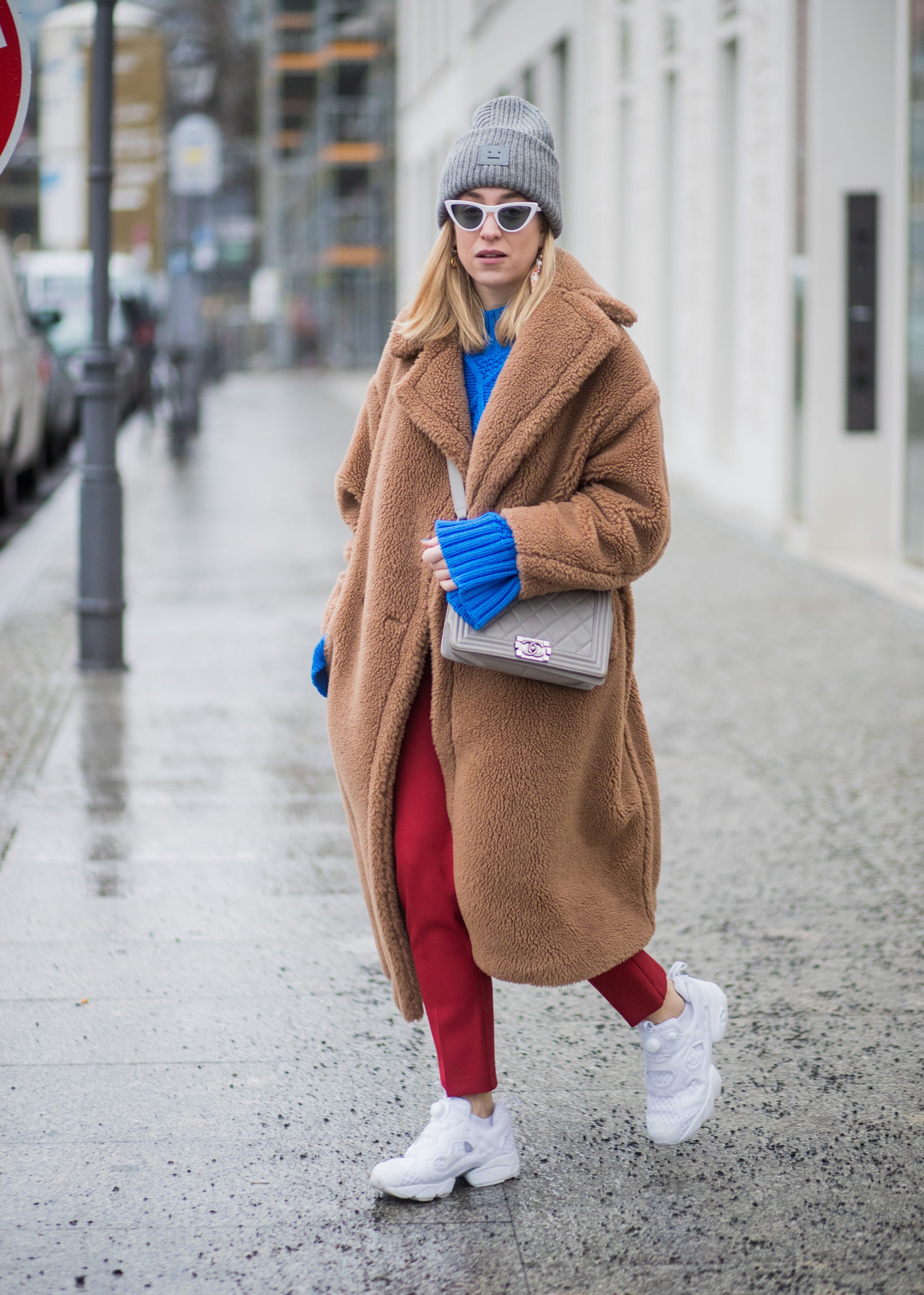 Woman wearing a tan teddy coat with a cobalt blue knit, red trousers and white sneakers