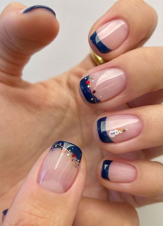 Short round nails with navy French tips, colorful confetti dots and a snowman accent nail
