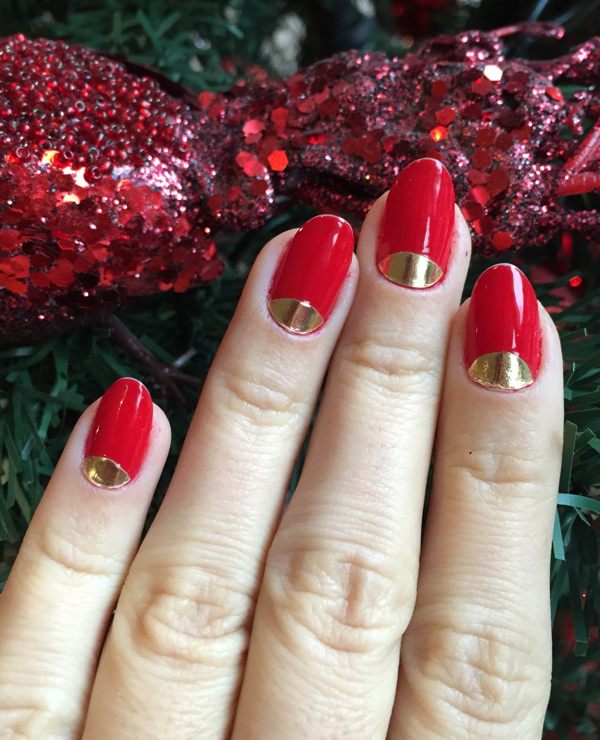Short oval red nails with gold foil half-moons at the cuticles