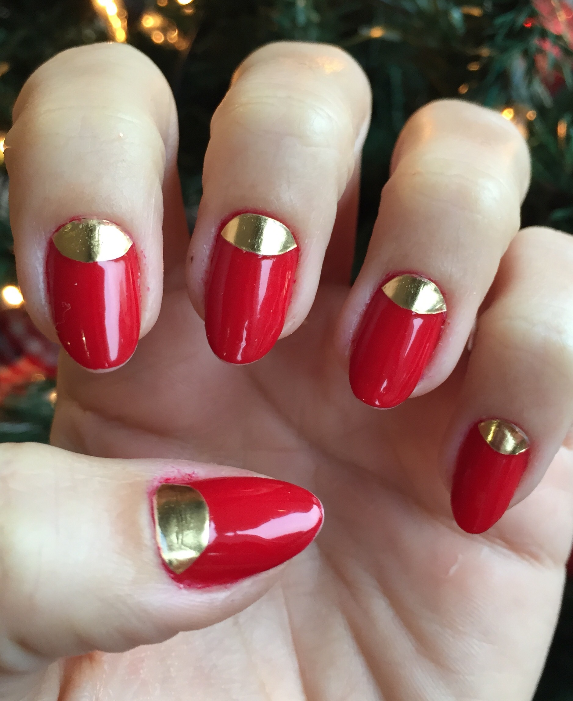 Red almond nails with a gold half-moon detail at the cuticle