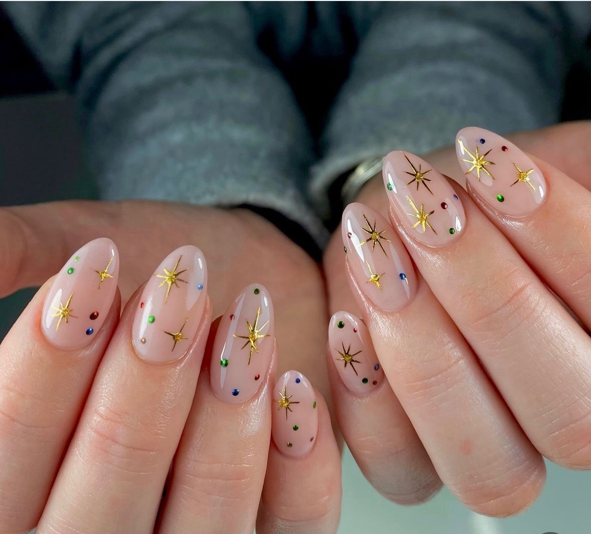 Short sheer nude Christmas nails with gold starburst art and colorful dots