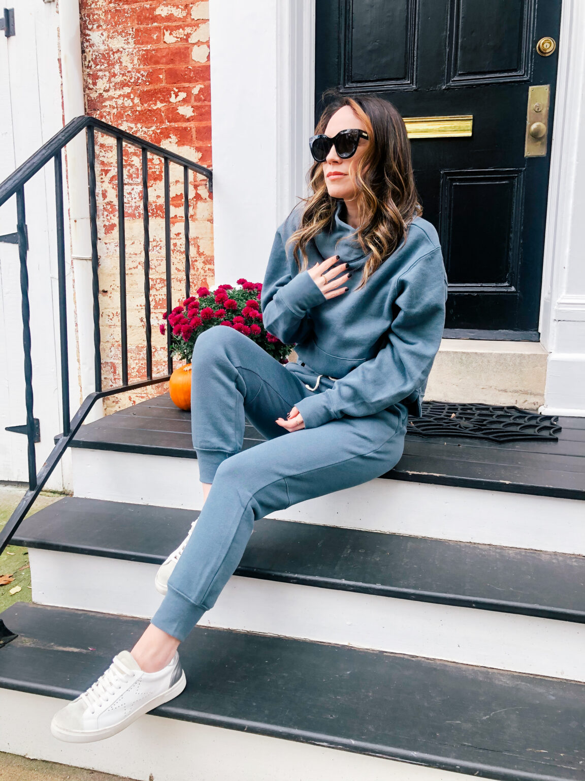Woman in a dusty blue cowl-neck sweatshirt with matching blue joggers and white sneakers