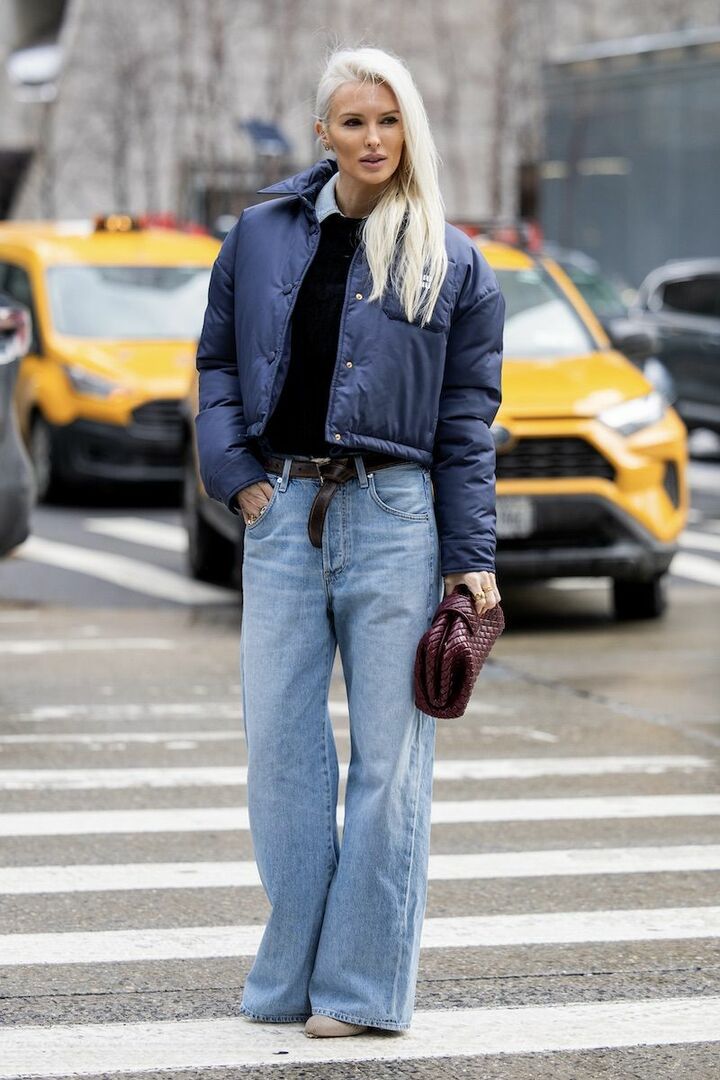 Cropped navy quilted puffer jacket with wide-leg jeans and a woven clutch