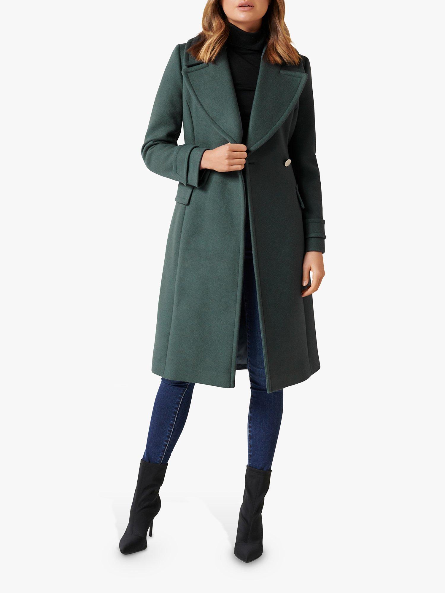 Woman wearing a forest green wrap wool coat with black turtleneck, dark jeans and black ankle boots