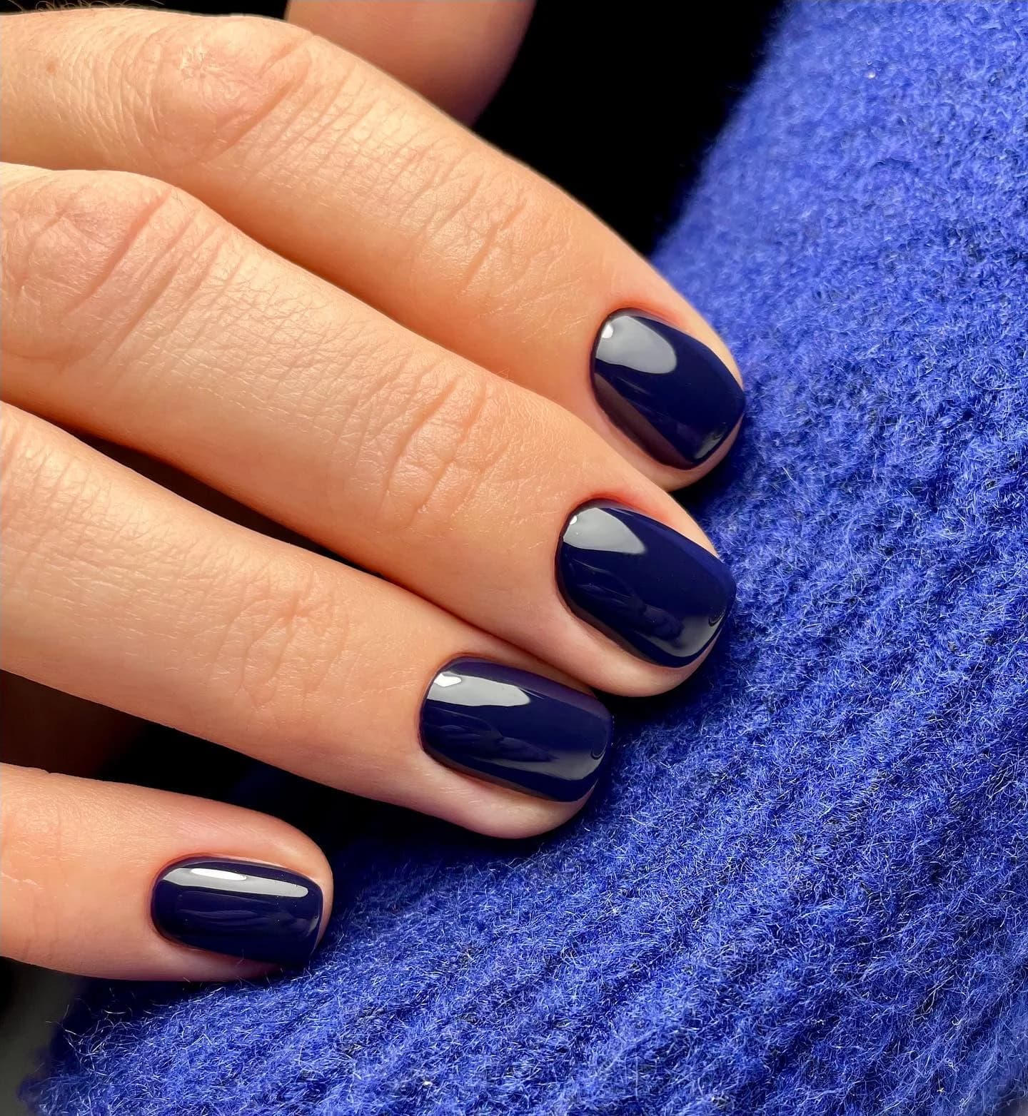 Navy blue creme nail polish on short nails against a blue knit sweater