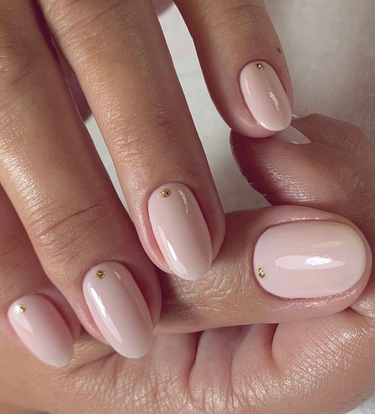 Almond nails with nude polish and a tiny gold dot accent at each cuticle