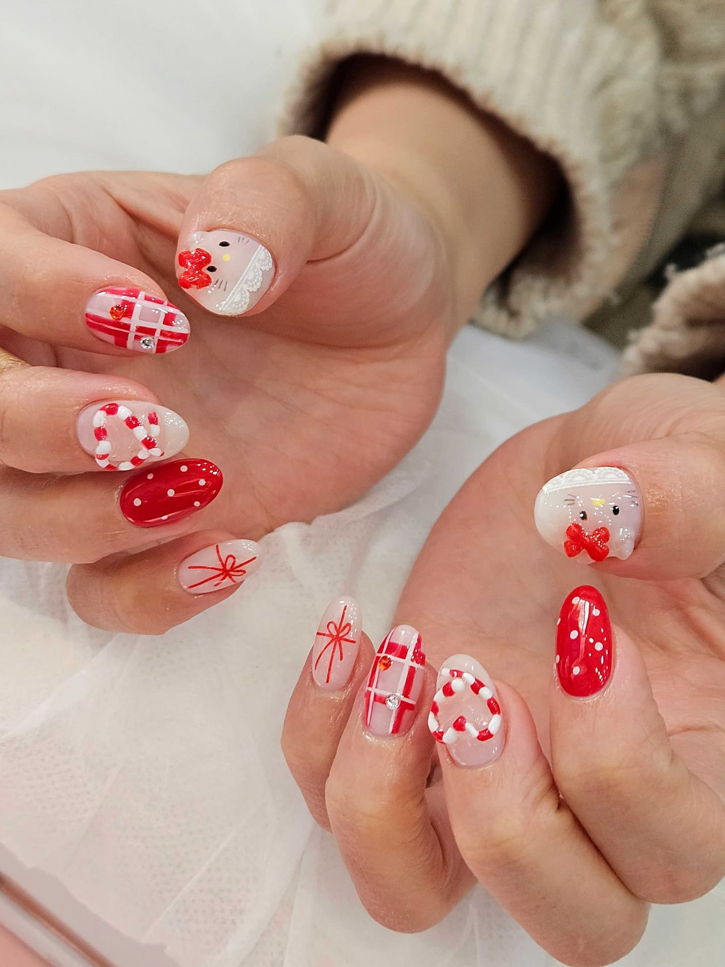 Short oval nails in sheer nude with red check plaid, candy cane hearts, red polka dots, Hello Kitty faces with 3D red bows and lace tips