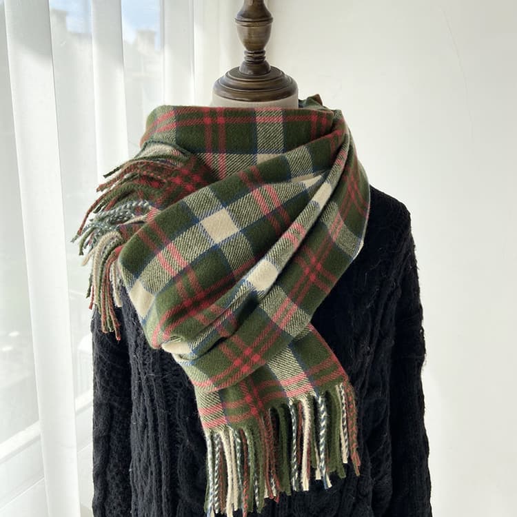 Green and red plaid fringed scarf draped over a black cable knit sweater
