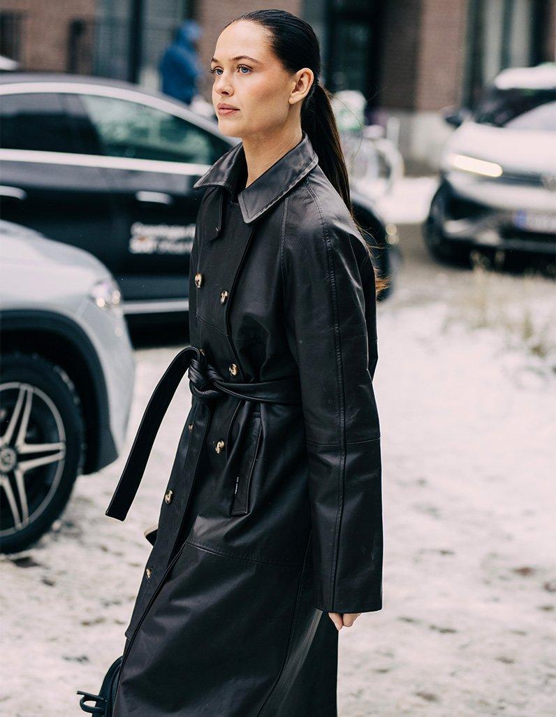 Woman wearing a belted black leather trench coat on a snowy city street
