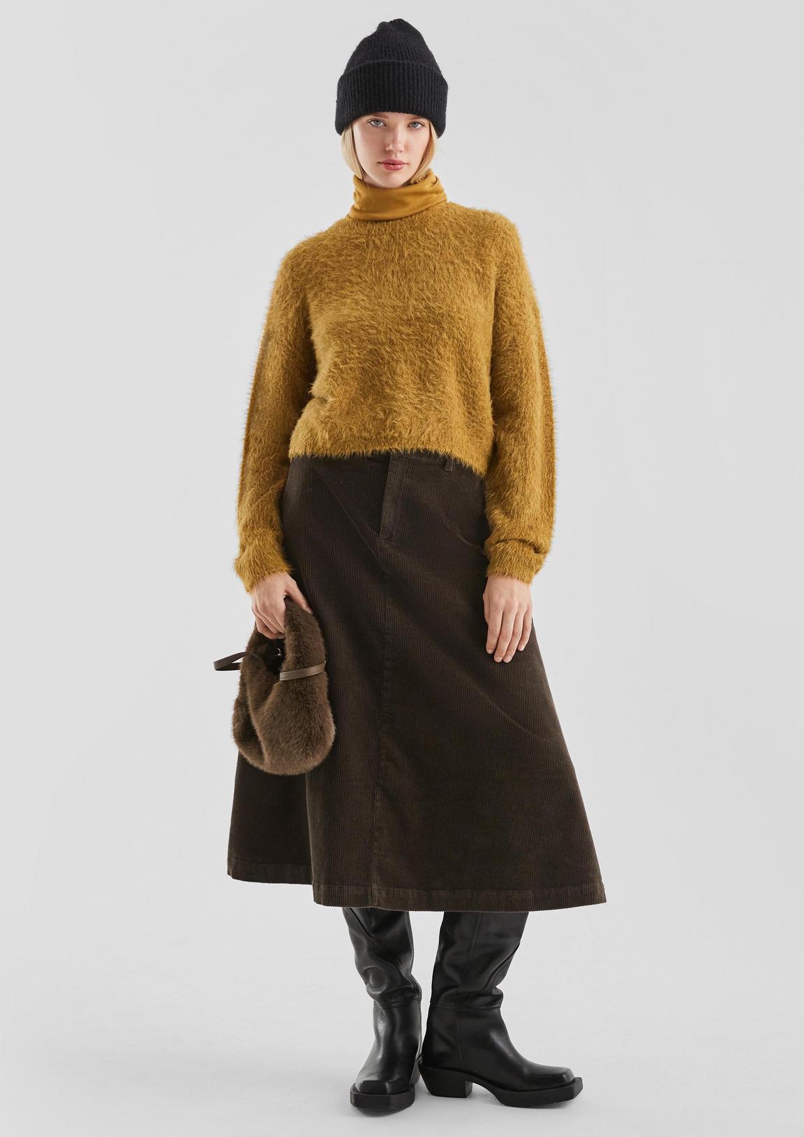 Woman in a black beanie, mustard fuzzy turtleneck and brown corduroy skirt