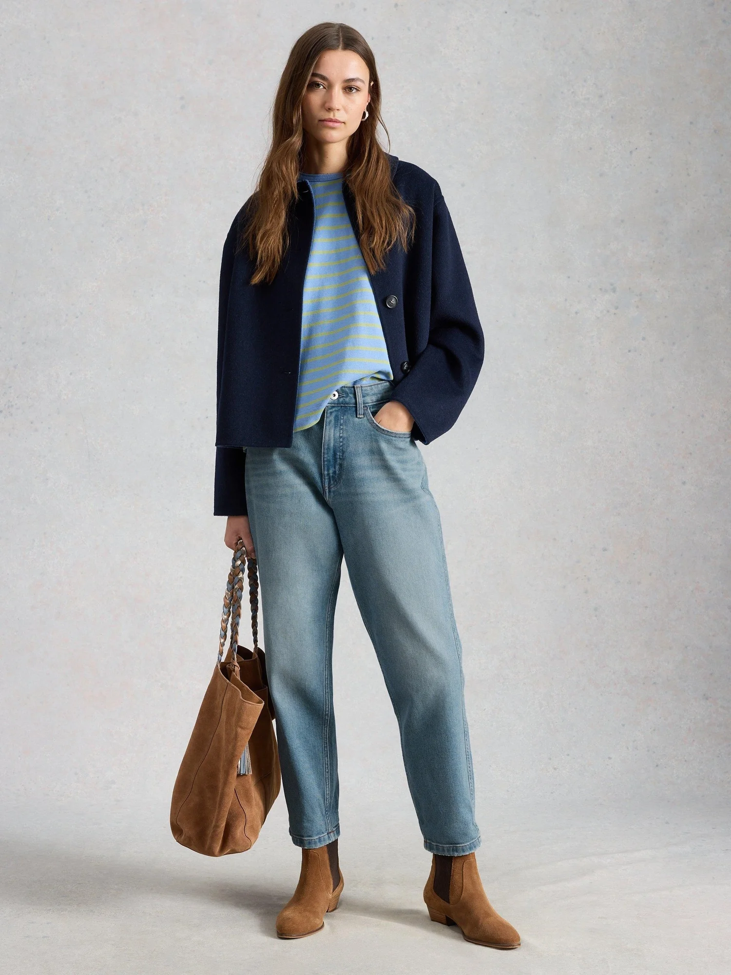 Woman wearing a navy cropped wool jacket, striped tee, straight jeans and tan suede chelsea ankle boots