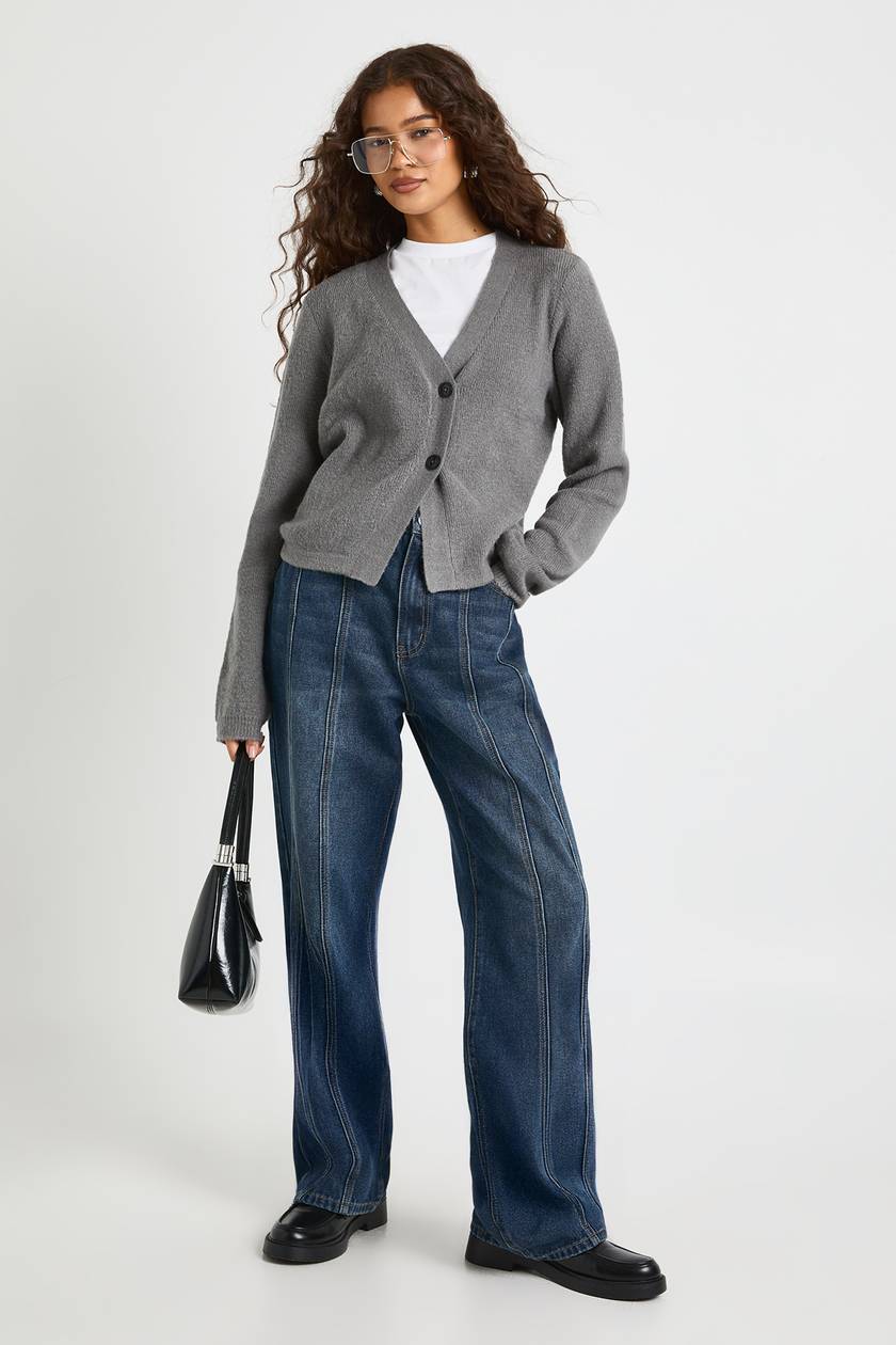Woman wearing a grey V-neck cardigan over a white t-shirt with dark wide-leg jeans, black loafers and a black handbag