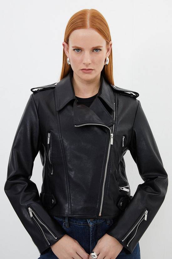 A cropped black biker jacket in smooth faux leather with silver zips and snap detailing over dark blue jeans.