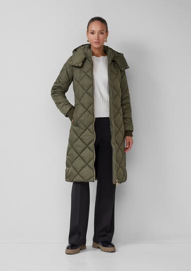 An olive quilted longline coat with a hood, worn over a white top and black wide-leg trousers with loafers.
