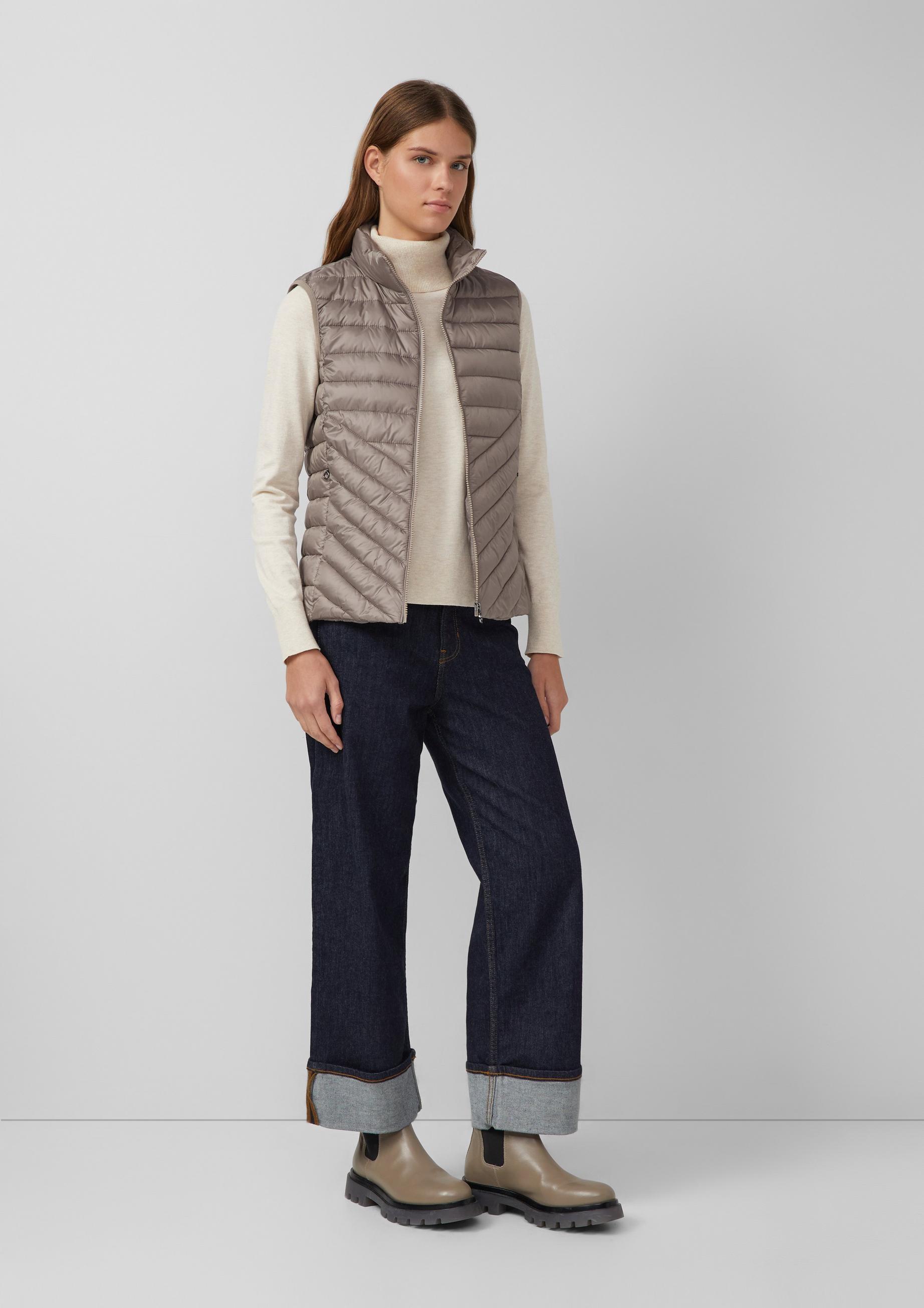 Woman in a taupe quilted vest, cream turtleneck, cuffed wide jeans and taupe Chelsea boots