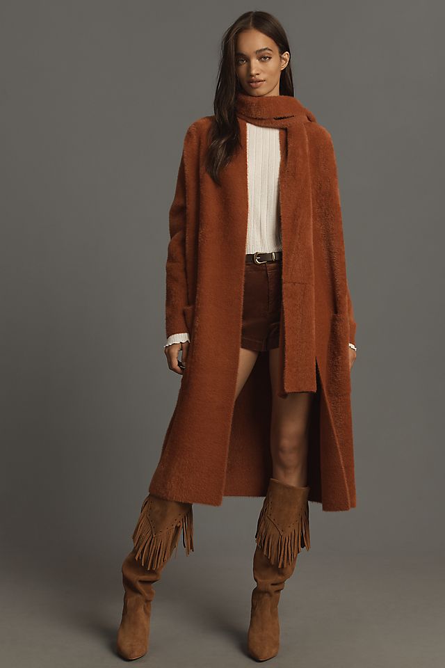 Model in a rust-colored fuzzy long coat with a matching scarf, cream top and fringe suede boots