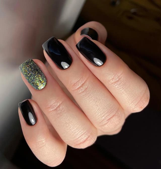 Glossy black nails with one nail fully covered in multicolor glitter