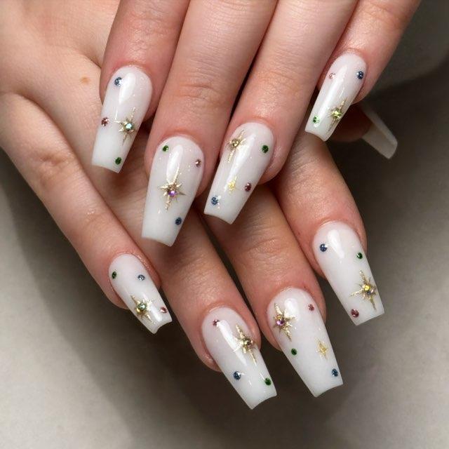 Long square milky white nails with gold starburst decals and tiny multicolor rhinestones