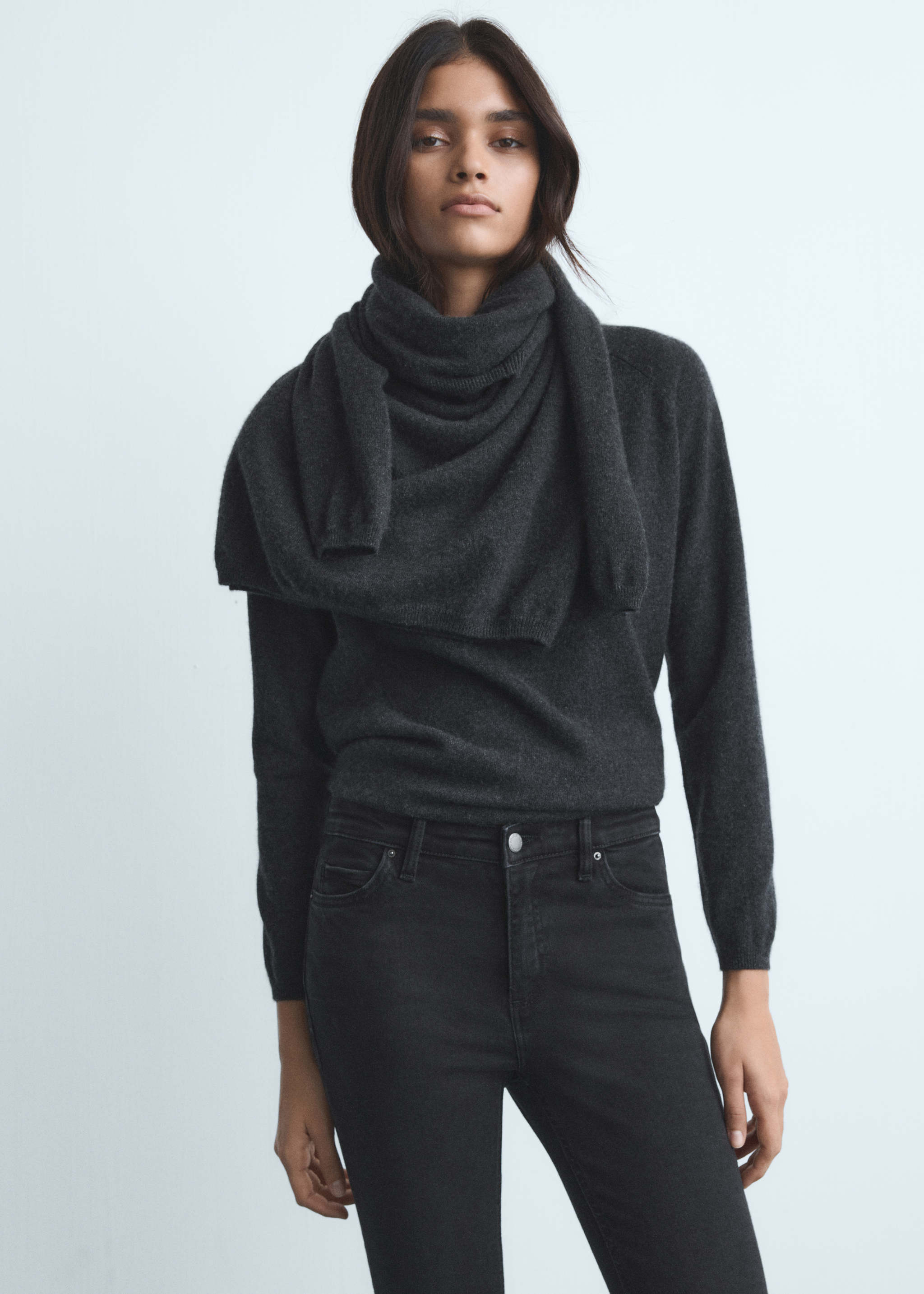 Woman in a dark grey knit sweater with a draped knit shawl and black skinny jeans