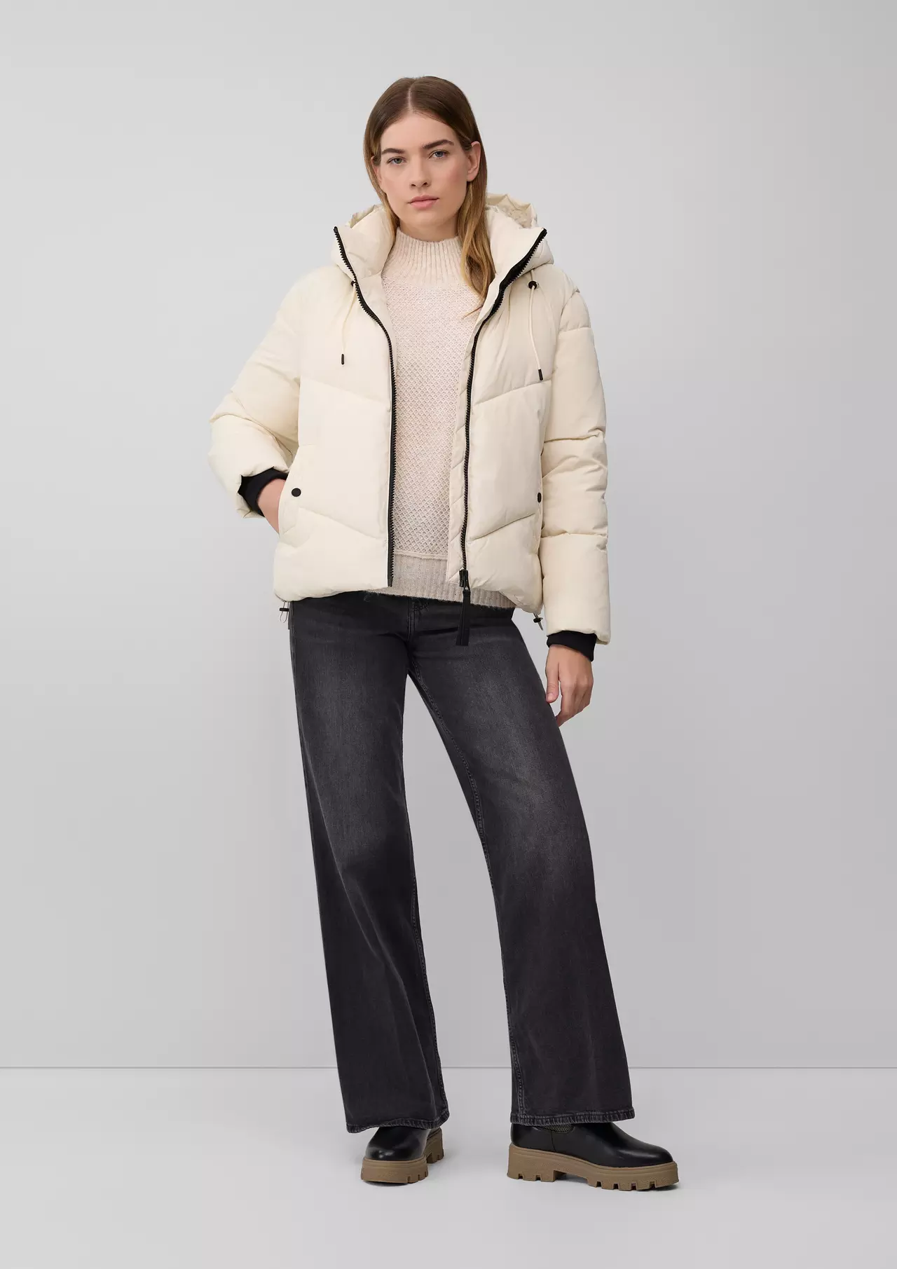 Woman in a cream puffer jacket and knit over black wide-leg jeans with chunky black boots