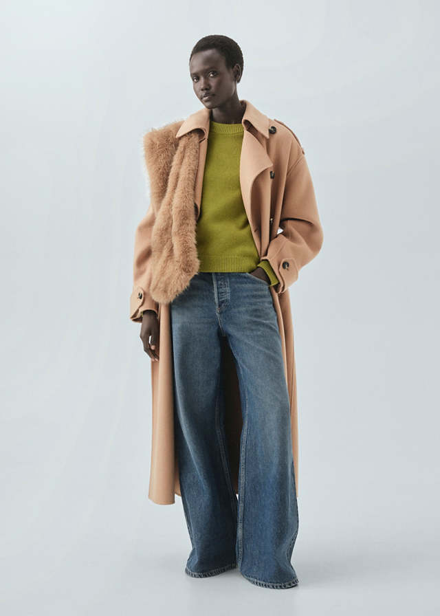 Woman in a camel coat with faux-fur lapels over a chartreuse knit and medium-wash wide-leg jeans